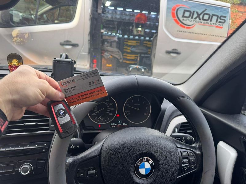 A new BMW key held up inside the customer's car, with our van parked outside